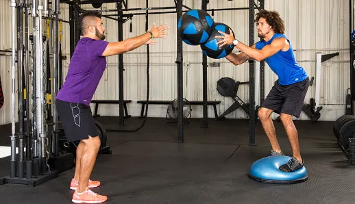 Two men are practicing their moves on a bosu ball.