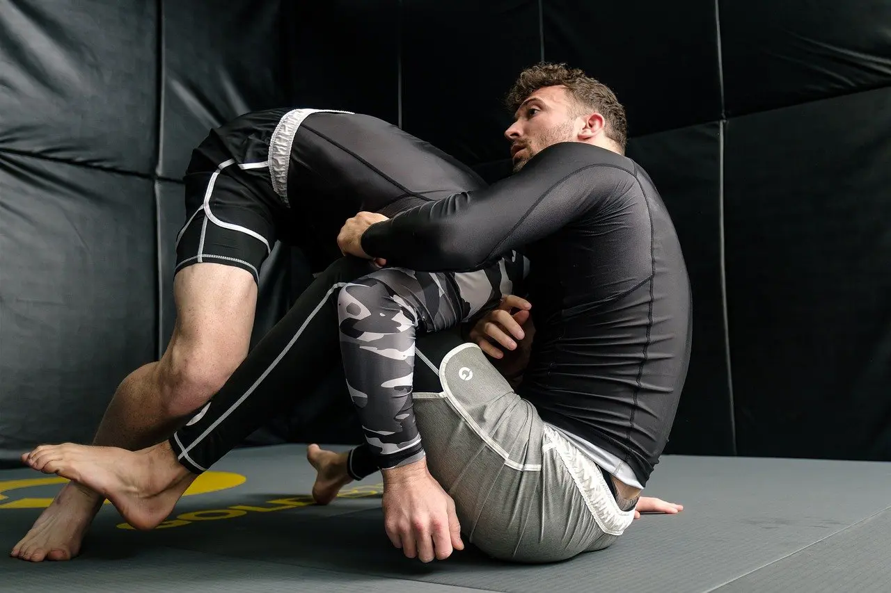 Two men are wrestling on a mat in the gym.