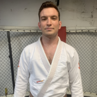 A man in white shirt and black belt standing next to fence.