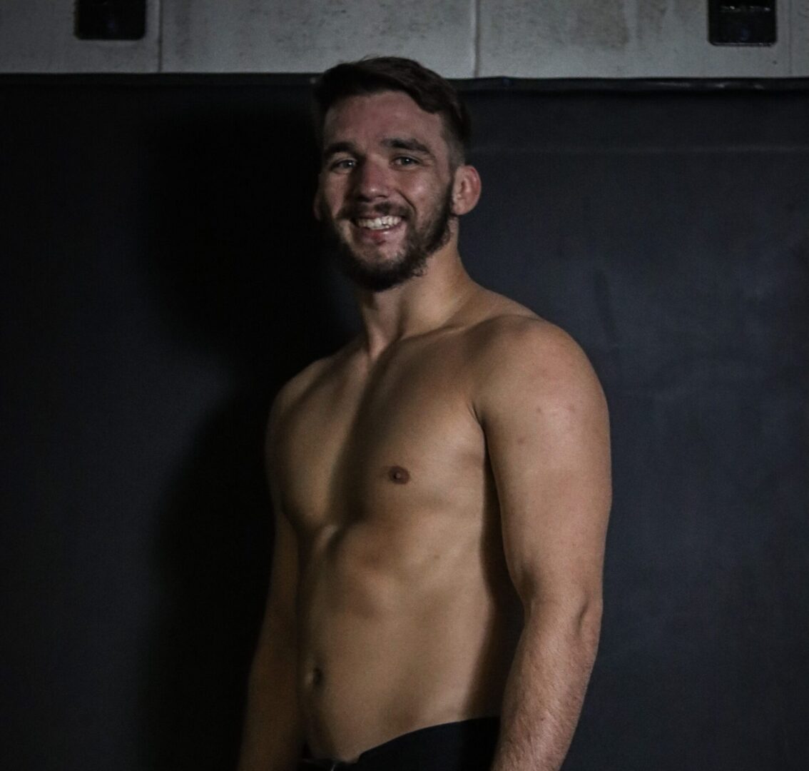 A man standing in front of a wall with his shirt off.